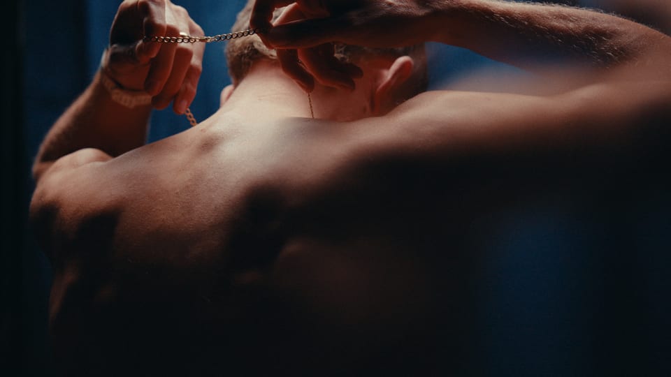 Athlete's bare back as he fastens a chain, lit in blue and warm tones