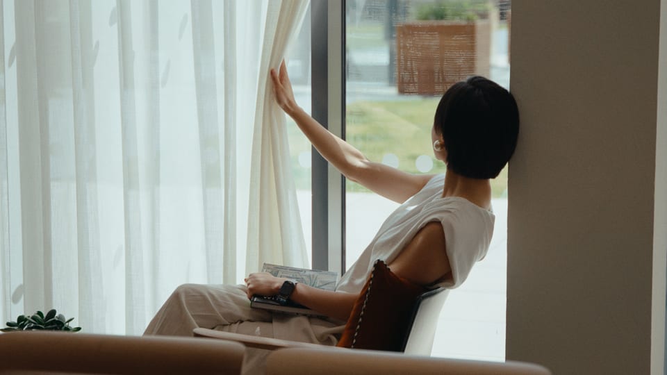Woman sitting by a tall window with sheer curtains