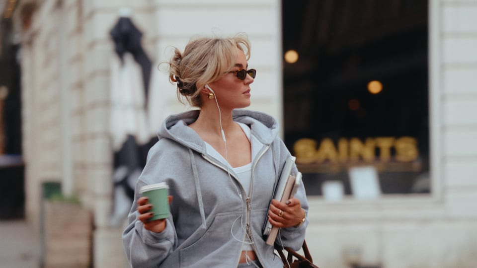 Woman in a grey hoodie and sunglasses with a coffee in the street