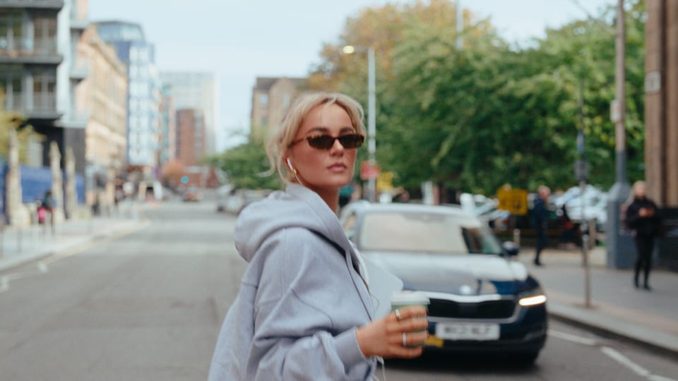 Woman in a grey hoodie and sunglasses on a city street